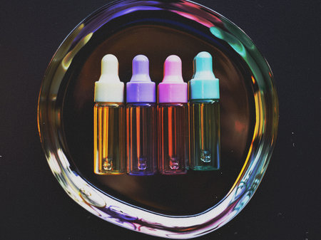 Rainbow dropper bottles on a reflective metal tray. Vibrant glass vials for essential oils or...
