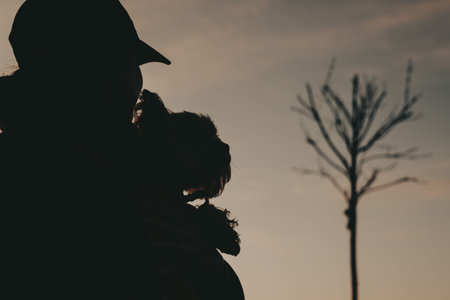 Silhouette of a woman holding a small Yorkshire terrier dog at sunset. Golden hour sky, emotional...