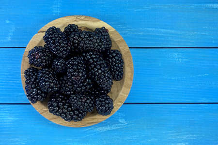 Ripe blackberries on a plate on a blue wooden backgroundの写真素材