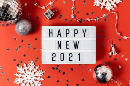 Happy new year 2021 table with modern light box with Christmas silver balls, white snowflakes and confetti.New year eve concept on redの写真素材