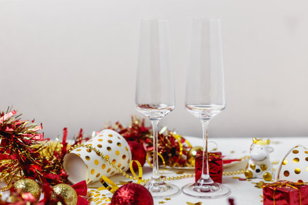 Festive table decoration, confetti stars, red decorative boxes, red shiny Christmas balls, gold ribbons with a glass of champagne on a white background. Holiday atmosphere.の写真素材