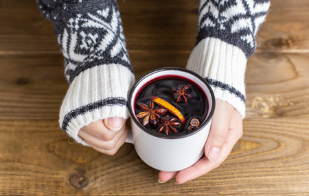 Composition with a mug of hot red mulled wine with spices in woman hands. Cozy holiday atmosphere, warm sweater, Christmas atmosphereの写真素材