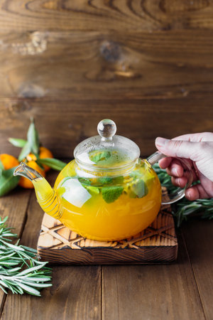 Hot tea with passionfruit and mint in a glass teapot, rosemary and miniature tangerines on the table, selective focus, rustic background, top viewの写真素材
