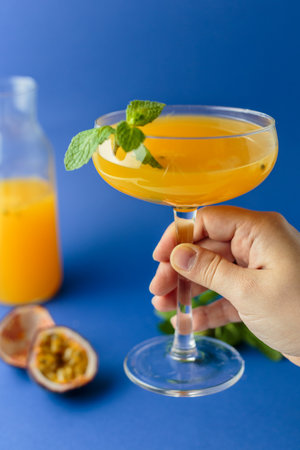 The passion fruit cocktail with mint and orange in glass on blue background in woman handの写真素材