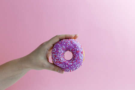 Crop female hand holding sweet pink donut isolated on pink backgroundの写真素材