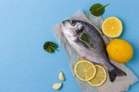 Raw dorado fish on baking paper with ingredients for cooking lemon, garlic and basil on blue...