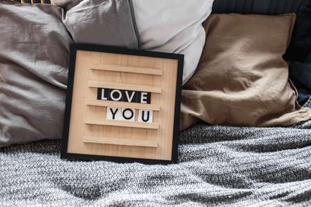 The inscription Love you on a wooden board on pillows on the bed with a gray bedspreadの写真素材