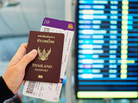 BANGKOK, THAILANDN - APR 14, 2016 : Hand holding Thailand Passport and Boarding Pass with flight schedule board Blur background. Airport departure terminalのeditorial素材
