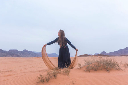A young woman with blond hair in a long dark blue dress is playing with sand. Wadi Rum Desert Jordanの写真素材