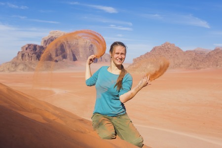 young woman with a smile sprinkled sand in the desertの写真素材