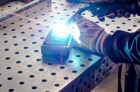 Worker with protective gloves welding steel on a welding table. Arc / MIG / MAG / solid-wire welding.の写真素材
