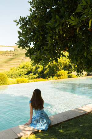 The girl in the dress rests by the pool on a sunny dayの写真素材