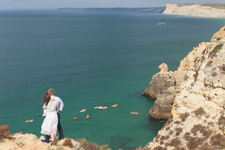 Young couple stands on a beautiful cliff and looks out at the ocean landscapeの写真素材