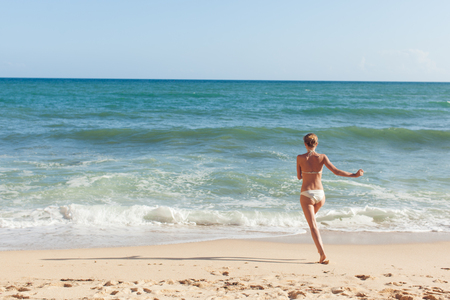 Happy Girl in swimsuit running along the beach to the waterの写真素材