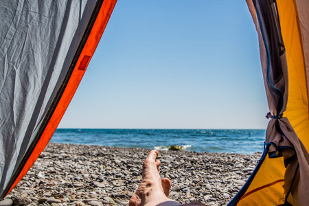 Image human legs lying in tourist tent with view of the seaの写真素材
