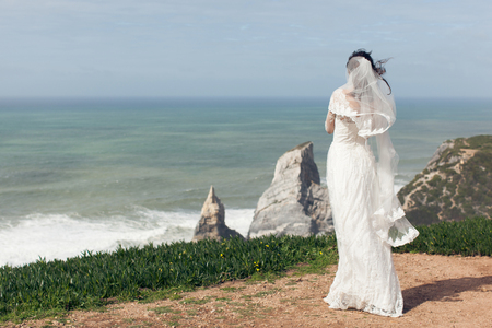 Bride in a beautiful white dress on a cliff by the ocean close-upの写真素材