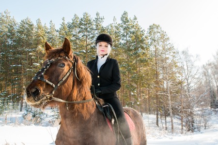Young beautiful girl jockey riding a horse in winter forestの写真素材