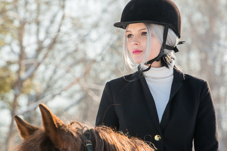 Portrait of young girl jockey riding a horse in winter forestの写真素材