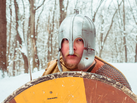Medieval Irish warrior in chain mail and helmet holds a shield in the winter forestの写真素材