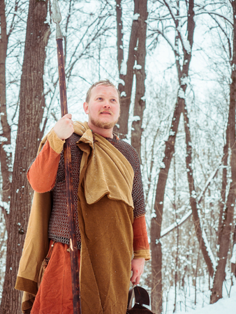 Medieval Irish warrior in chain mail and helmet holds a spear in the winter forestの写真素材
