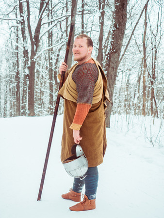 Medieval Irish warrior in chain mail and helmet holds a spear in the winter forestの写真素材
