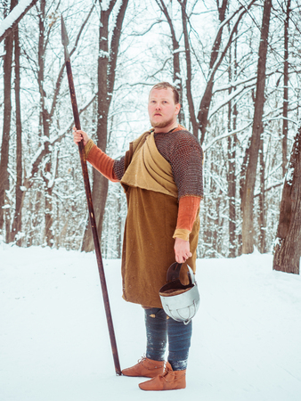 Medieval Irish warrior in chain mail and helmet holds a spear in the winter forestの写真素材
