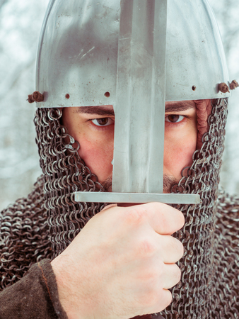 Medieval viking warrior in chain mail and helmet holds a sword in the winter forestの写真素材