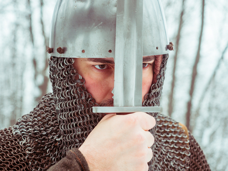 Medieval viking warrior in chain mail and helmet holds a sword in the winter forestの写真素材