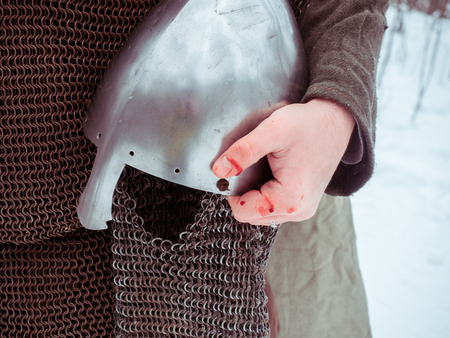 Medieval viking warrior in chain mail holds a helmet in his hand in the winter forestの写真素材