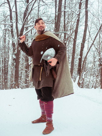 Medieval viking warrior in chain mail and helmet holds a sword in the winter forestの写真素材