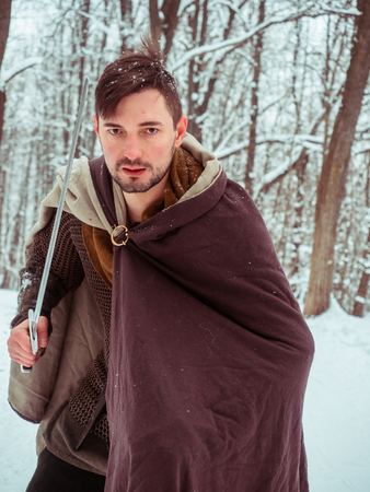 Medieval viking warrior in chain mail and helmet holds a sword in the winter forestの写真素材