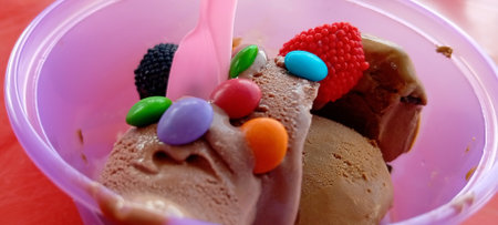 Ice cream scoops in plastic container with spoon and colorful candiesの写真素材