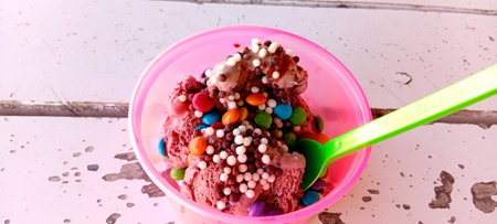 Colorful ice cream in a pink plastic cup on a wooden tableの写真素材