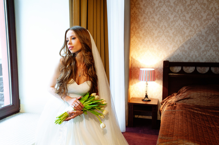 Bride in wedding dress at luxurious suites, a luxury apartment near window with flowersの写真素材