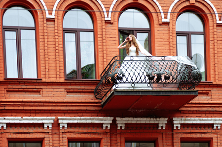 Bride in wedding dress on balcony of luxury apartment at the red hotel buildingの写真素材