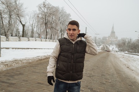 Outdoor winter portrait for young handsome man. Beautiful teenager in his jacket and vest posing on a city street, background of town. Colorの写真素材