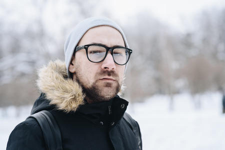 Profile of attractive happy young man with beard standing in winter forest. Glasses, jacket, hat. Color.の写真素材