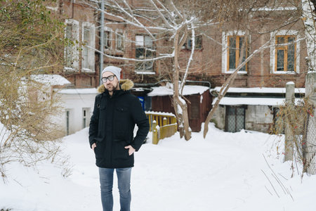 Profile of attractive happy young man with beard standing in winter urban. Glasses, jacket, hat. Color.の写真素材