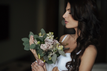 Naked girl sitting on the bed in a beautiful position and touches her long hair. Interior hotel room with large windows. Color.の写真素材