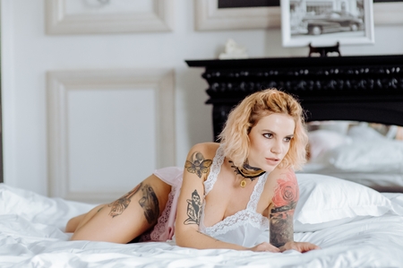 Beautiful bride with tattoo in lingerie showing sexy pose leaning at bed over her bedroom. Color. Sexual memories.の写真素材