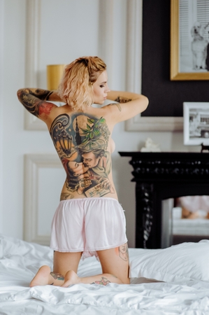 Beautiful bride with tattoo in lingerie showing sexy pose standing at bed over her bedroom. Sexual memories.の写真素材