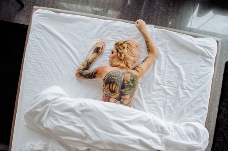 Beautiful bride with tattoo in lingerie showing sexy pose leaning at bed over her bedroom. Color. Sexual memories. Pictures on spin.の写真素材