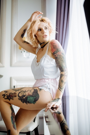 Beautiful bride with tattoo in lingerie showing sexy pose, sitting at table over her bedroom. Color. Sexual memories.の写真素材