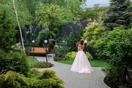 Outdoor summer portrait of young pretty cute girl with flouwers on her hands. Beautiful bride posing at outdoor. Woman in rose wedding dess standing in park near old building. Photo has gorgeus model.の写真素材