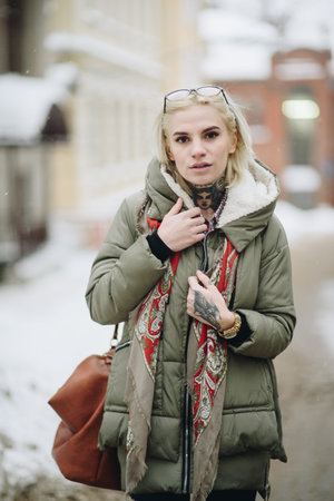 Outdoor portrait of young beautiful happy girl posing on street. Model wearing stylish warm clothes. Magic snowfall. Winter holidays concept. City lifestyle. Waist up. Colorの写真素材