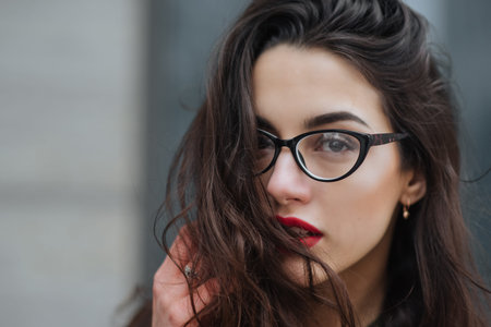 Fashion consept: beatiful young girl with long hair, glasses, red lips standing near modern wall wearing in green suit and grey jeans. She wanted talking on phone. Colorの写真素材