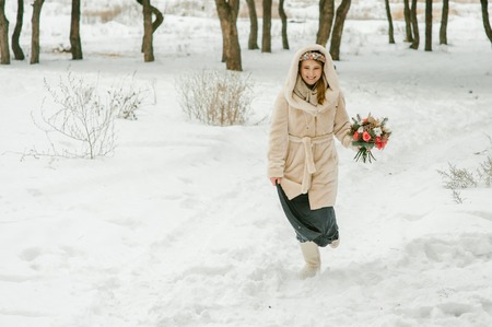 Outdoor happy bride in love posing in cold winter. Young girl having fun outdoor. Charming girl. Attractive young woman with flower bouquet runing forward and smilingの写真素材