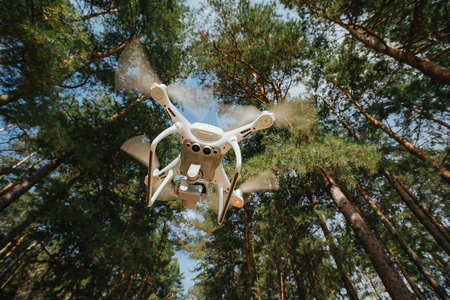 Modern drone in motion. Quadcopter with 4K camera flying in forest. Drone aerial photography concept.の写真素材