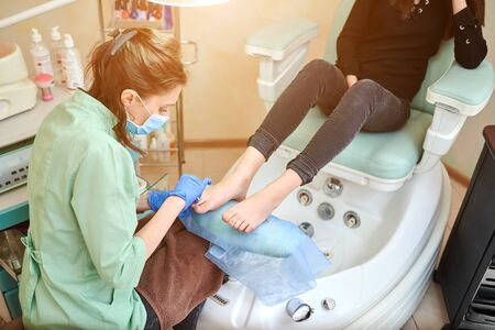 Pedicure for a woman in the nail salon. Master using professional instruments when doing a procedure. Patient on medical procedure, visiting podiatrist. Foot treatment in SPA salon. Podiatry clinic.の写真素材