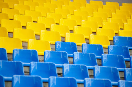 Rows of yellow and blue seats chairs in a stadiumの写真素材